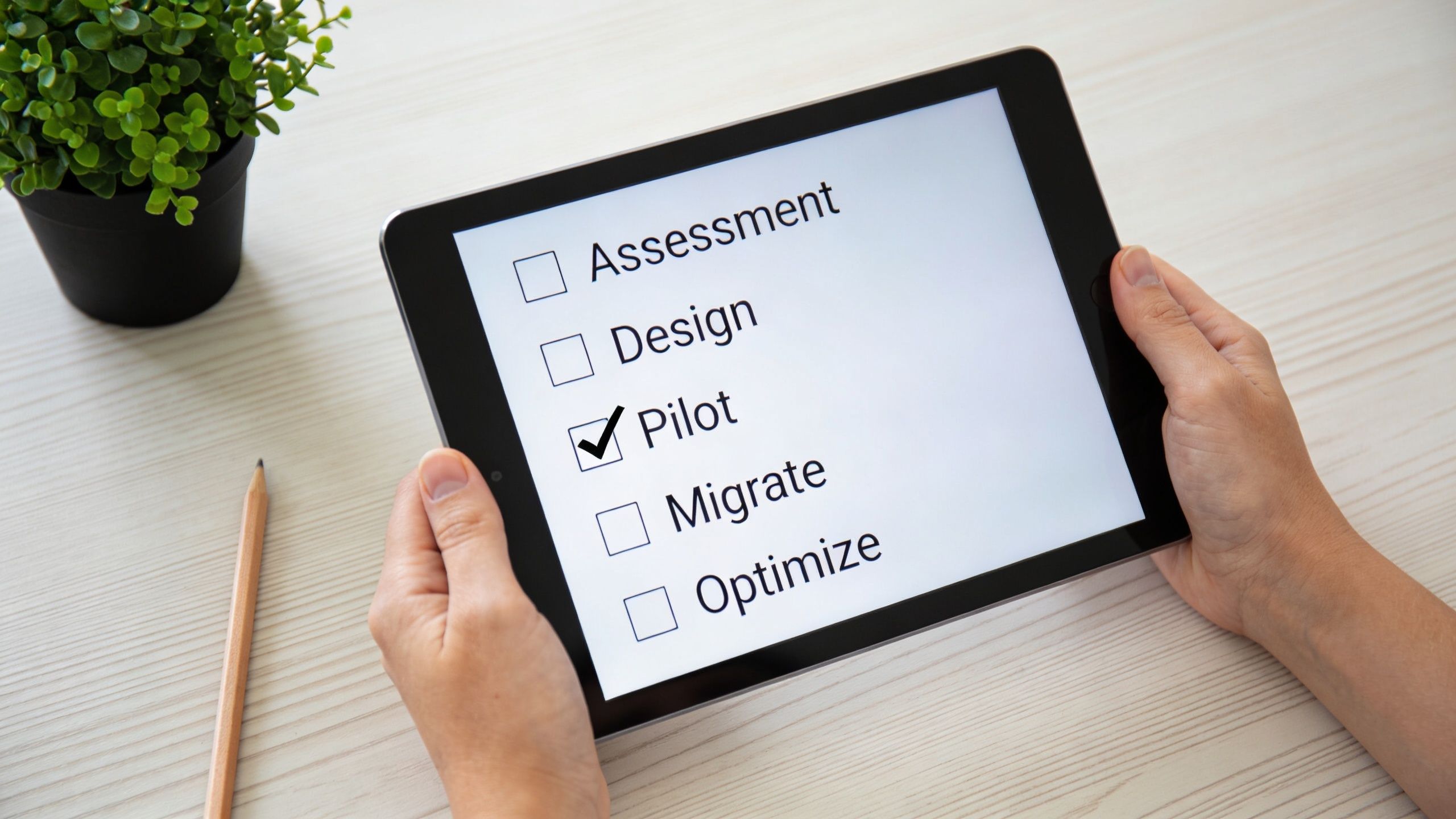 A person holding a tablet showing a checklist for cloud migration steps including assessment, design, and pilot.
